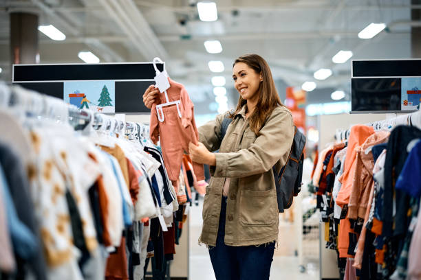 Young happy woman choosing baby clothes at the store