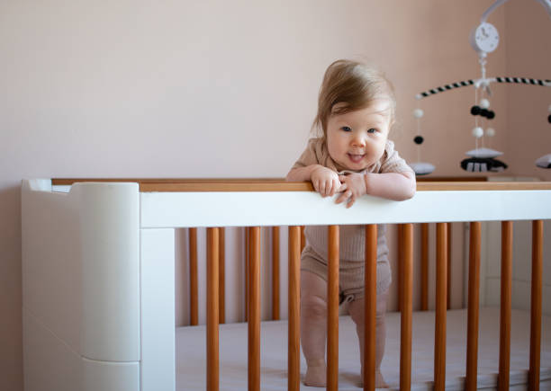 cute Caucasian baby girl 6 months old standing in a crib and looking at the camera