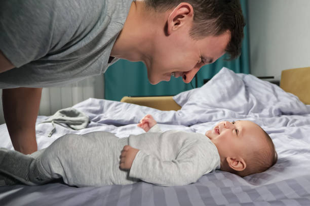 Baby wearing soft white cotton bodysuit smiling on a bed.