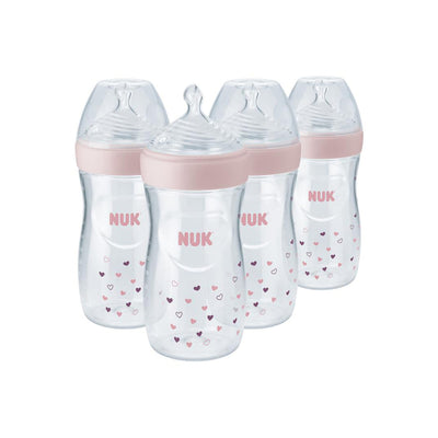 Four NUK baby bottles with pink caps and heart patterns on a white background
