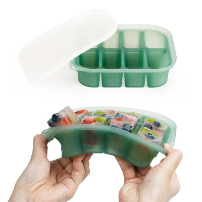 Green silicone ice cube tray with frozen fruit cubes held by hands on a white background