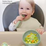 Baby using a green self-feeding tool with a bowl of food, sitting in a high chair.