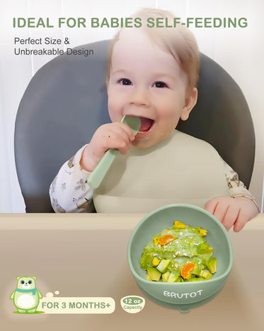 Baby using a green self-feeding tool with a bowl of food, sitting in a high chair.