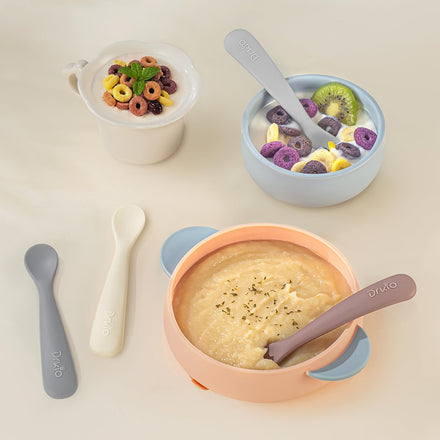 Assorted baby feeding bowls and spoons with different food items on a light background