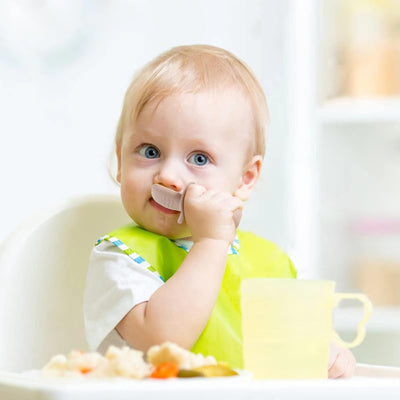 Baby sitting in a high chair with a bib, surrounded by food and a cup.