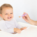 Child sitting in a high chair with a spoon held by an adult, on a white background