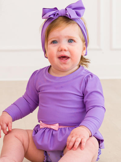 RuffleButts Baby Girls UPF50+ Princess Long Sleeve Bow Skirted One Piece Swimsuit - Amethyst Princess, 18-24m