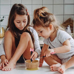 Two young girls sitting on the floor eating from a bowl with utensils.