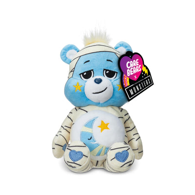 Plush toy bear with blue face and white body, wearing a bandage, on a white background with 'Care Bears' tag.