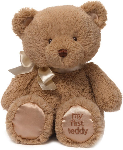 Brown teddy bear with a bow and 'my first teddy' tag on a white background
