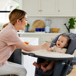 Woman feeding a baby in a high chair in a kitchen.