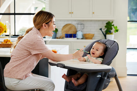 Woman feeding a baby in a high chair in a kitchen.
