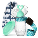 Clear baby bottle with green cap and blue strap, featuring a patterned bag in the background.