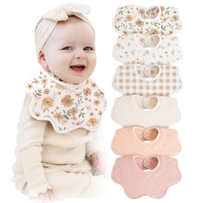 Baby wearing a floral bib with a stack of similar bibs on a white background